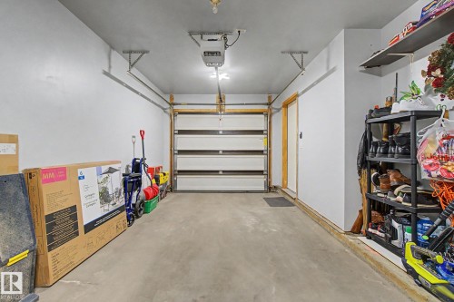 Attached garage with a sectional garage door, concrete flooring, white painted walls, and built-in shelving - 210 401 Southfork Drive, Leduc, AB - Indoor Photo Showing Garage