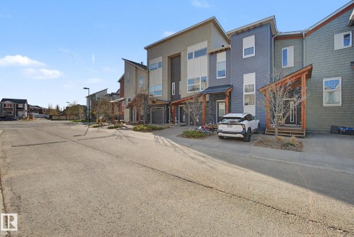 Modern townhome featuring a multi-story facade with varied siding textures, a covered entry porch, dark trim accents, and a distinctive sloped roofline - 210 401 Southfork Drive, Leduc, AB - Outdoor