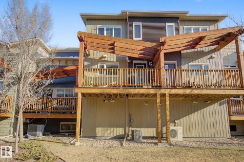 Multi-level townhome featuring a rear wooden deck with a pergola, exterior siding in varying shades, and ground-level gravel landscaping - 210 401 Southfork Drive, Leduc, AB - Outdoor With Balcony With Exterior