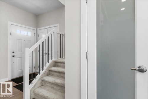 Entry foyer featuring wood-finish flooring, a carpeted staircase with white newel posts and black metal balusters, and a white paneled front door with an upper transom window - 2847 Koshal Crescent, Edmonton, AB - Indoor Photo Showing Other Room