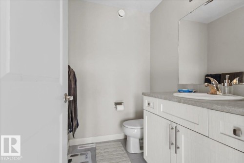 Bathroom featuring a single vanity with white cabinetry, a textured countertop, an integrated sink, and a wall-mounted mirror - 2847 Koshal Crescent, Edmonton, AB - Indoor Photo Showing Bathroom