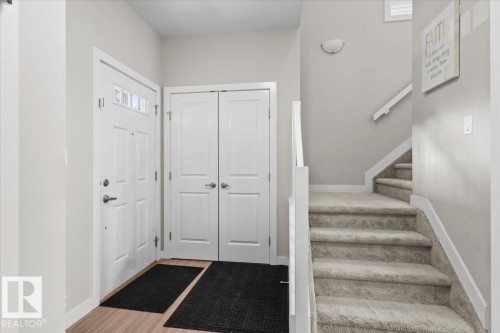 Entryway featuring a paneled door with transom window, wood-finish flooring, bi-fold doors, and a carpeted staircase with white railing - 2847 Koshal Crescent, Edmonton, AB - Indoor Photo Showing Other Room