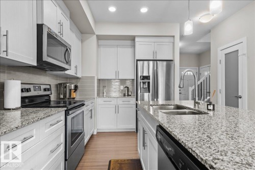 Modern kitchen featuring granite countertops, stainless steel appliances, white cabinetry, and wood-finish flooring - 2847 Koshal Crescent, Edmonton, AB - Indoor Photo Showing Kitchen With Stainless Steel Kitchen With Double Sink With Upgraded Kitchen