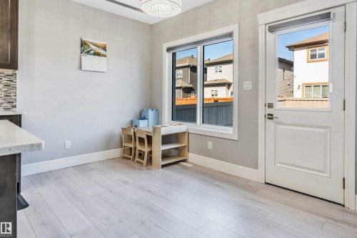 Light wood-finish flooring extending from the kitchen area, featuring a door with an inset window and a rectangular window offering exterior views - 1103 29 Street, Edmonton, AB - Indoor