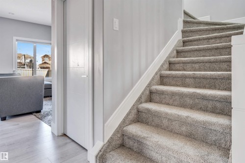 Carpeted staircase with white trim, featuring a contemporary white door, light-toned wood-finish flooring, and a bright window - 1103 29 Street, Edmonton, AB - Indoor Photo Showing Other Room