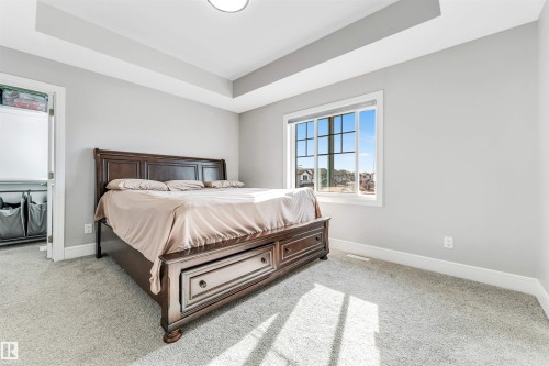 Carpeted room featuring a tray ceiling, a large window with white trim, and a white baseboard - 1103 29 Street, Edmonton, AB - Indoor Photo Showing Bedroom
