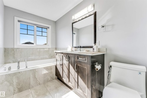 Bathroom featuring a built-in tub with tile surround, a single vanity with stone countertop, and a large framed mirror - 1103 29 Street, Edmonton, AB - Indoor Photo Showing Bathroom