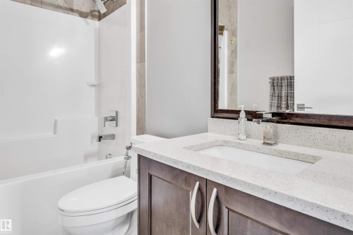 Bathroom featuring a dark wood vanity with a white composite countertop, an integrated rectangular sink, a framed mirror, and a white tub with a shower combo - 1103 29 Street, Edmonton, AB - Indoor Photo Showing Bathroom