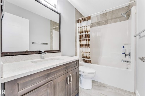 Bathroom featuring a wood-finish vanity with a white composite countertop and integrated sink, a large framed mirror, a white toilet, and a white tub/shower combination with tile surround - 1103 29 Street, Edmonton, AB - Indoor Photo Showing Bathroom