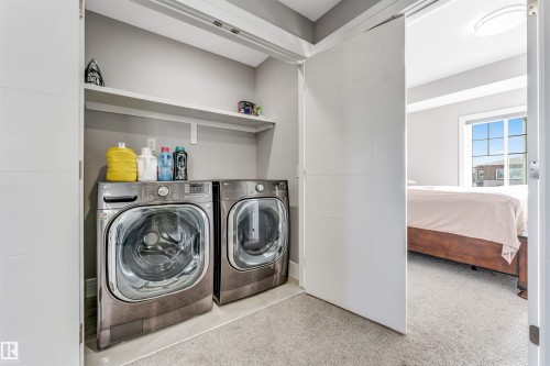 Dedicated laundry area featuring a front-loading washer and dryer set, an overhead storage shelf, and a light gray wall finish - 1103 29 Street, Edmonton, AB - Indoor Photo Showing Laundry Room