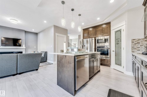 Open-concept kitchen featuring an island with pendant lighting, stainless steel appliances, wood-finish flooring, and a pantry with a frosted glass door - 1103 29 Street, Edmonton, AB - Indoor Photo Showing Kitchen With Upgraded Kitchen