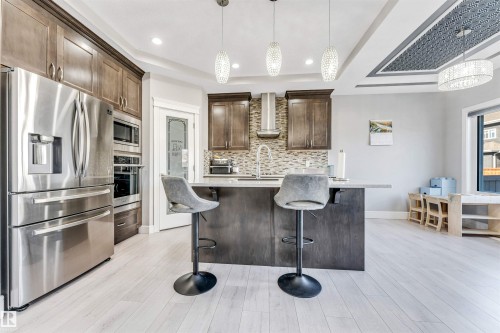 Gourmet kitchen featuring stainless steel appliances, wood cabinetry, a central island with counter seating, a mosaic tile backsplash, and light wood-finish flooring - 1103 29 Street, Edmonton, AB - Indoor Photo Showing Kitchen With Upgraded Kitchen