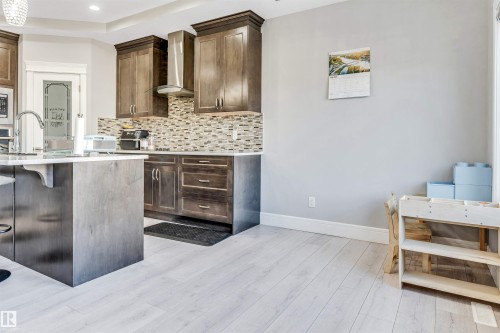 Contemporary kitchen featuring wood-finish cabinetry, a patterned tile backsplash, and light wood-finish flooring - 1103 29 Street, Edmonton, AB - Indoor Photo Showing Kitchen With Upgraded Kitchen