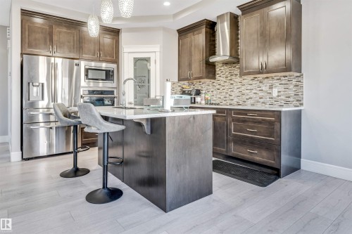 Modern kitchen featuring dark wood-finish cabinetry, stainless steel appliances, a center island with bar seating, a mosaic tile backsplash, and light wood-finish flooring - 1103 29 Street, Edmonton, AB - Indoor Photo Showing Kitchen With Upgraded Kitchen