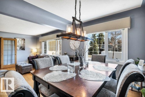 Dining area featuring a dark wood-finish dining table with upholstered chairs, a rectangular chandelier with glass shades, and light wood-finish flooring - 10616 136 Street, Edmonton, AB - Indoor