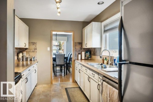 Galley kitchen featuring light cabinetry, a stainless steel refrigerator, tile backsplash, and a window above the sink - 10616 136 Street, Edmonton, AB - Indoor Photo Showing Kitchen With Double Sink