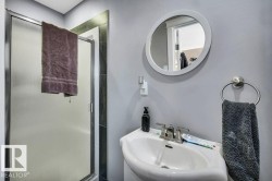 Bathroom featuring a stand-up shower with a frosted glass door, a pedestal sink with a chrome faucet, a circular wall mirror, and a wall-mounted towel ring - 