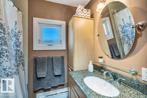 Bathroom featuring a granite countertop vanity with an oval sink, a wall-mounted oval mirror, and a wood-finish storage cabinet - 10616 136 Street, Edmonton, AB - Indoor Photo Showing Bathroom
