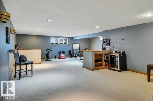 Spacious lower-level room featuring light-toned carpeting, recessed ceiling lighting, and a built-in bar with open shelving - 10616 136 Street, Edmonton, AB - Indoor