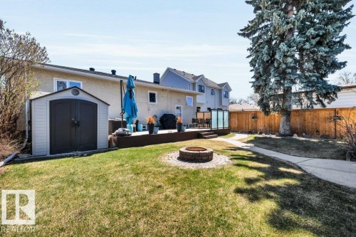 Expansive backyard featuring a large elevated deck with glass panel railings, a stone-ringed fire pit, manicured lawn, and mature trees - 10616 136 Street, Edmonton, AB - Outdoor