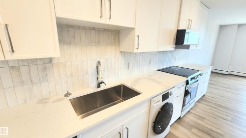 Modern kitchen featuring white cabinetry with brushed nickel hardware, light-toned countertop, and a vertical subway tile backsplash - 603 9028 Jasper Avenue, Edmonton, AB - Indoor Photo Showing Kitchen