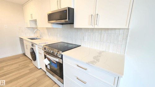 Modern kitchen featuring white cabinetry, light-toned countertops with subtle veining, stainless steel appliances, and a stacked subway tile backsplash - 603 9028 Jasper Avenue, Edmonton, AB - Indoor Photo Showing Kitchen With Upgraded Kitchen