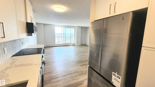 Kitchen featuring white cabinetry with brushed nickel hardware, light-toned countertops, a glass cooktop, and a stainless steel refrigerator - 603 9028 Jasper Avenue, Edmonton, AB - Indoor Photo Showing Kitchen