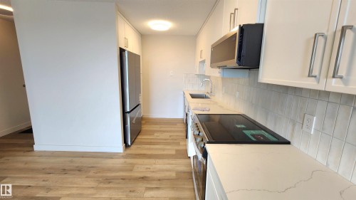 Modern kitchen featuring white cabinetry with silver-toned hardware, light wood-finish flooring, white countertop, and stainless steel appliances including a refrigerator, microwave, and electric range - 603 9028 Jasper Avenue, Edmonton, AB - Indoor Photo Showing Kitchen