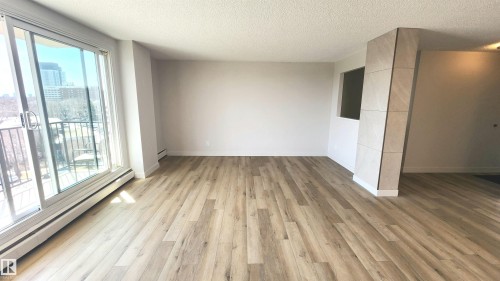 Spacious interior featuring wood-finish flooring and a full-height sliding glass door leading to a balcony - 603 9028 Jasper Avenue, Edmonton, AB - Indoor Photo Showing Other Room