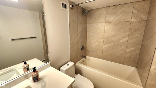 Bathroom featuring a full vanity with an integrated sink, a rectangular mirror, a chrome towel bar, and a tub-shower combination with floor-to-ceiling tile surround - 603 9028 Jasper Avenue, Edmonton, AB - Indoor Photo Showing Bathroom