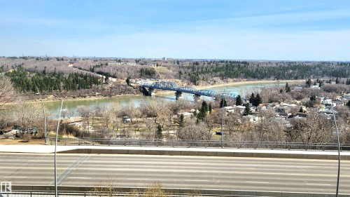 Riverfront landscape featuring a blue steel bridge, distant residential structures, and extensive wooded areas under a clear sky - 603 9028 Jasper Avenue, Edmonton, AB - Outdoor With View