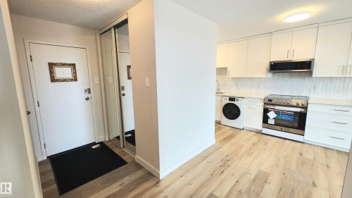 Modern kitchen featuring light wood-finish flooring, white cabinetry, and stainless steel appliances - 603 9028 Jasper Avenue, Edmonton, AB - Indoor