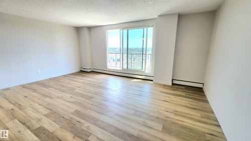 Spacious room featuring wood-finish flooring, light-colored walls, and a large sliding glass door with a balcony - 603 9028 Jasper Avenue, Edmonton, AB - Indoor Photo Showing Other Room