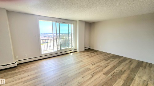 Spacious room featuring wood-finish flooring, light neutral wall paint, and a textured ceiling - 603 9028 Jasper Avenue, Edmonton, AB - Indoor Photo Showing Other Room