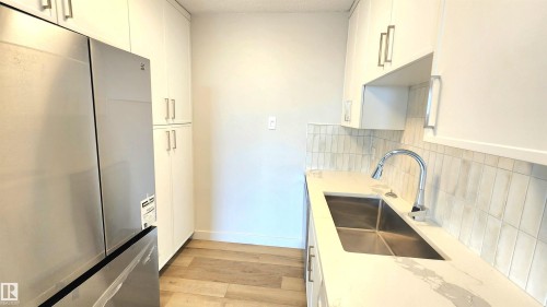 Bright kitchen featuring white cabinetry, a stainless steel refrigerator, and wood-finish flooring - 603 9028 Jasper Avenue, Edmonton, AB - Indoor Photo Showing Kitchen