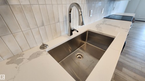 Stainless steel undermount sink with a high-arc chrome faucet, set into a white countertop with gray veining - 603 9028 Jasper Avenue, Edmonton, AB - Indoor