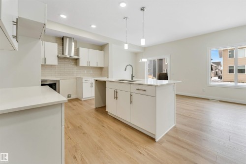 The kitchen features an island with a sink, white cabinetry with silver hardware, and recessed lighting - 97 Dansereau Way, Beaumont, AB - Indoor Photo Showing Kitchen With Upgraded Kitchen