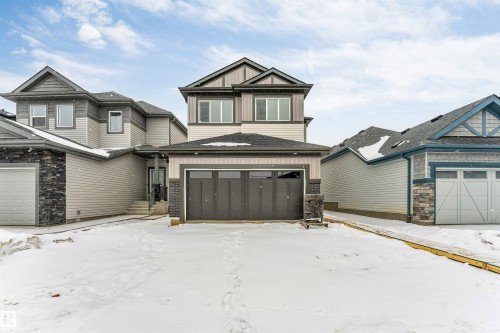 The property features a two-story exterior with light-colored siding, dark trim, and stone accents - 97 Dansereau Way, Beaumont, AB - Outdoor With Facade