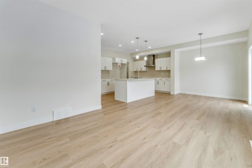 The property features an open-concept layout with light-toned flooring, a kitchen with white cabinetry, a central island, and modern pendant lighting - 97 Dansereau Way, Beaumont, AB - Indoor Photo Showing Kitchen