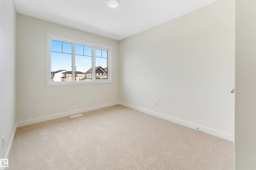 This bright room features neutral-toned carpet and walls, a large window with white trim, and a ceiling-mounted light fixture - 97 Dansereau Way, Beaumont, AB - Indoor Photo Showing Other Room