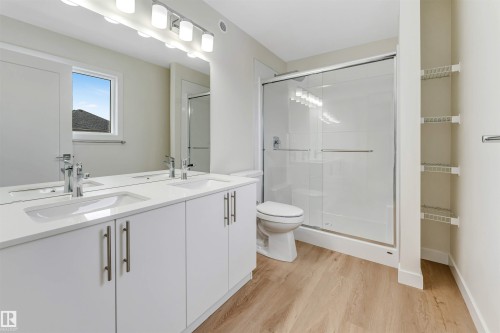 Bathroom featuring a double vanity with white cabinets and chrome fixtures, a shower with a sliding glass door, and light wood-style flooring - 97 Dansereau Way, Beaumont, AB - Indoor Photo Showing Bathroom