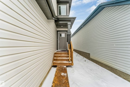 The property features neutral-toned siding, a dark grey entry door with a window, and wooden steps leading to the entrance - 97 Dansereau Way, Beaumont, AB - Outdoor With Exterior