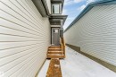 The property features neutral-toned siding, a dark grey entry door with a window, and wooden steps leading to the entrance - 97 Dansereau Way, Beaumont, AB  - Outdoor With Exterior 