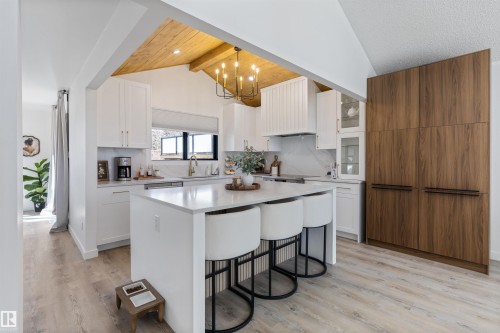 Modern kitchen featuring a central island with countertop seating, white shaker-style cabinetry, and wood-finish flooring - 38 Woodcrest Avenue, St. Albert, AB - Indoor Photo Showing Kitchen With Upgraded Kitchen