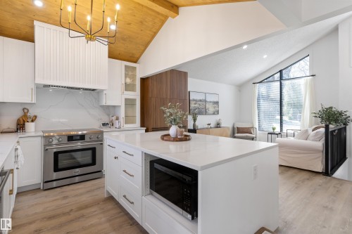 Open-concept kitchen featuring a large central island with quartz countertop, white cabinetry, stainless steel appliances, and wood-finish flooring - 38 Woodcrest Avenue, St. Albert, AB - Indoor Photo Showing Kitchen With Upgraded Kitchen