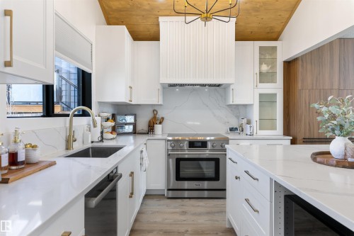 Gourmet kitchen featuring white cabinetry, quartz countertops, a stone slab backsplash, stainless steel appliances, and wood-finish flooring - 38 Woodcrest Avenue, St. Albert, AB - Indoor Photo Showing Kitchen With Upgraded Kitchen