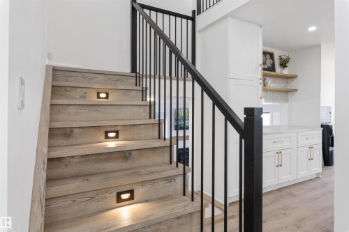 Modern staircase featuring wood-finish treads with integrated step lighting and a black iron railing - 38 Woodcrest Avenue, St. Albert, AB - Indoor Photo Showing Other Room