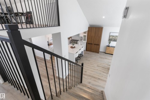 Contemporary black metal railings leading to a bright open-concept living space with vaulted ceilings, recessed lighting, wood-finish flooring, and a kitchen island with seating - 38 Woodcrest Avenue, St. Albert, AB - Indoor Photo Showing Other Room