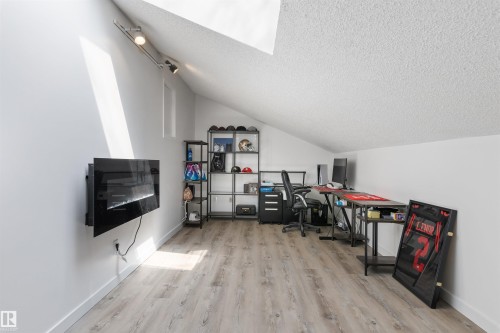 Attic space featuring wood-finish flooring, a wall-mounted fireplace, track lighting, and a sloped ceiling - 38 Woodcrest Avenue, St. Albert, AB - Indoor Photo Showing Other Room