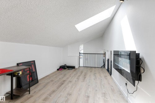 Spacious loft area featuring a vaulted ceiling with two skylights, light wood-finish flooring, a contemporary black metal railing, and a wall-mounted electric fireplace - 38 Woodcrest Avenue, St. Albert, AB - Indoor Photo Showing Other Room